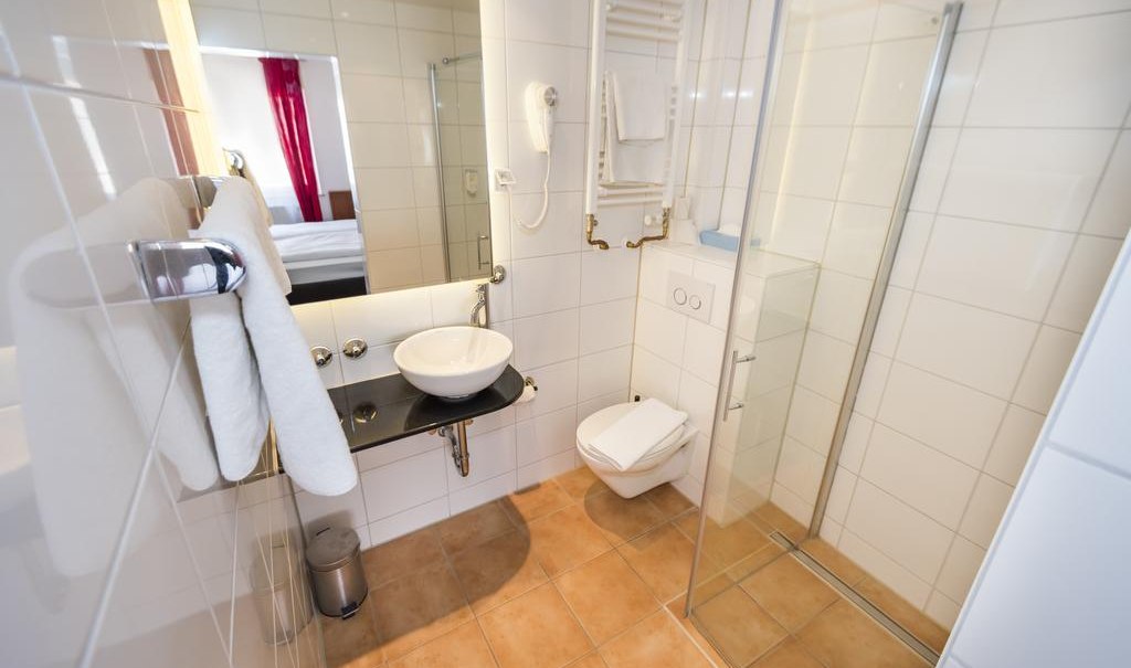 Modernes Badezimmer mit Glasdusche, Waschbecken, Handtüchern und Toilette. Weiße Fliesen und ein Spiegel sind sichtbar., © ARNOTEL GmbH Modernes Badezimmer mit Glasdusche, Waschbecken, Handtüchern und Toilette. Weiße Fliesen und ein Spiegel sind sichtbar., © ARNOTEL GmbH
