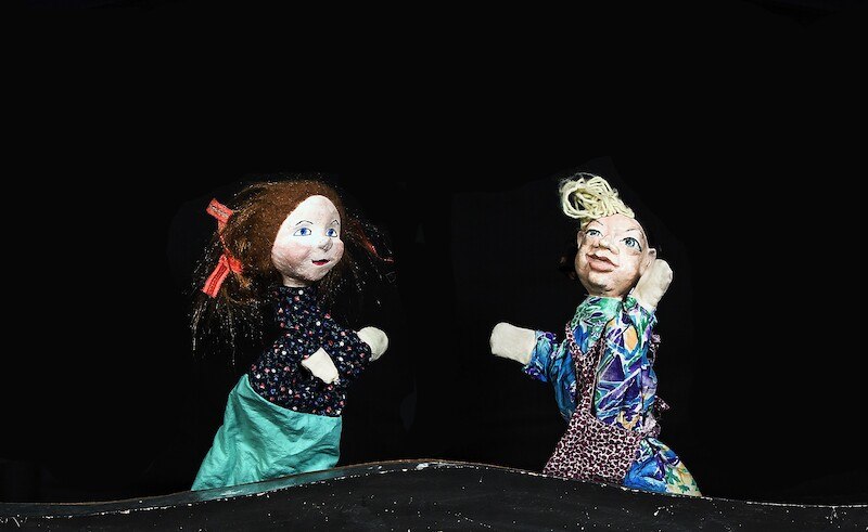 Zwei bunte Handpuppen mit fröhlichen Gesichtern auf einer dunklen Bühne. Eine Puppe hat rote Schleifen im Haar, die andere trägt ein gemustertes Outfit., © Prinzessin Gisela Theater