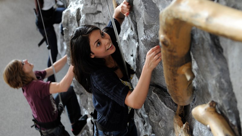 Zwei Personen klettern an einer Indoor-Kletterwand. Eine Frau lächelt, während sie die Wand erklimmt. Beide tragen Sicherheitsgurte., © Sensapolis Sindelfingen