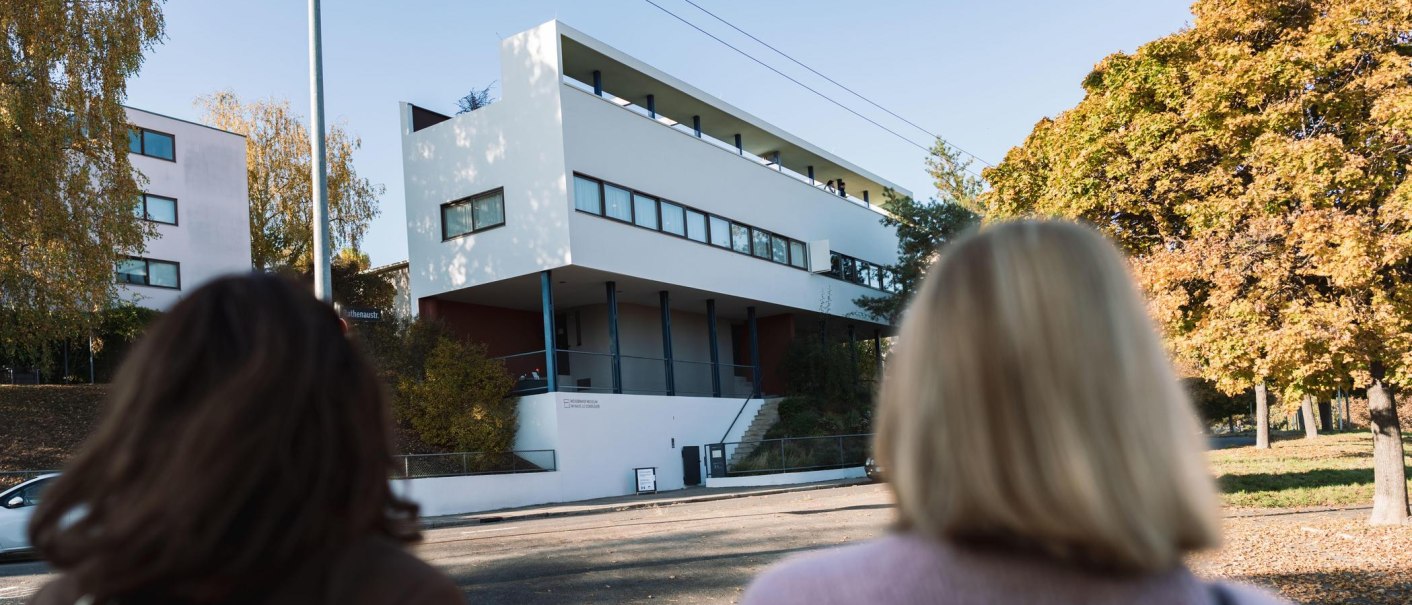 Zwei Personen betrachten das Haus Le Corbusier in der Weißenhofsiedlung. Modernes Gebäude mit klaren Linien, umgeben von herbstlichen Bäumen., © Stuttgart-Marketing GmbH, wpsteinheisser