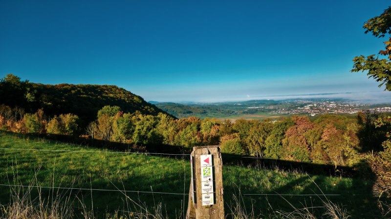 Panoramablick von der Maierhalde auf ein gr&uuml;nes Tal und eine Stadt in der Ferne. Ein Holzpfosten mit Wanderwegmarkierungen steht im Vordergrund., &copy; Landkreis G&ouml;ppingen