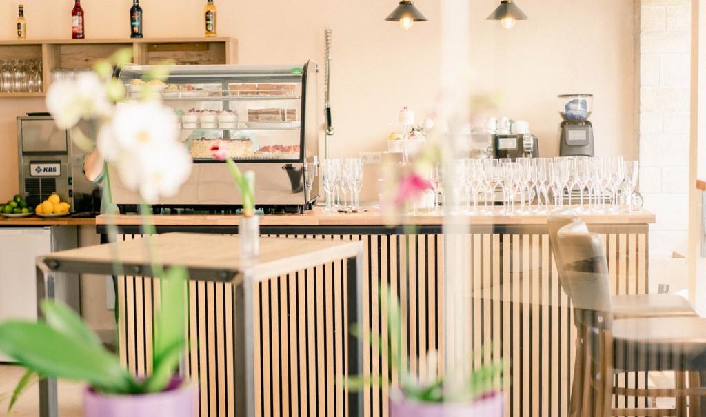 Ein stilvolles Caf&eacute; mit einer modernen Theke, Barhockern und Orchideen im Vordergrund. Im Hintergrund sind Gl&auml;ser und Flaschen zu sehen., &copy; cMagnolia