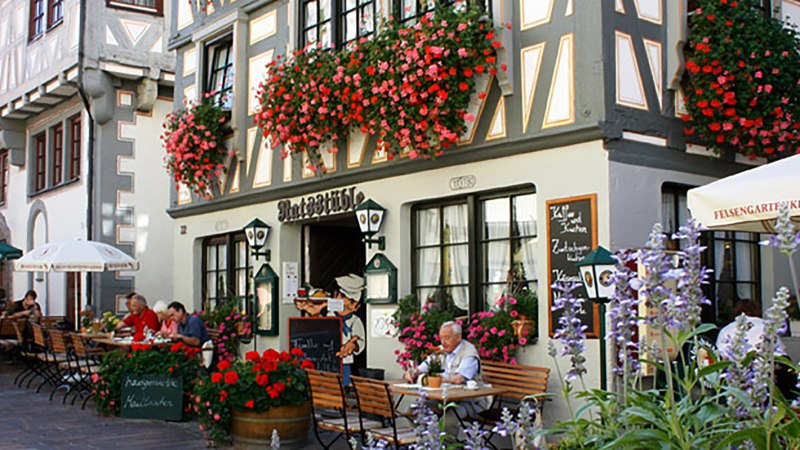 Fachwerkhaus in Besigheim mit Restaurant 'Ratsst&uuml;ble'. Menschen sitzen drau&szlig;en unter Sonnenschirmen, umgeben von bl&uuml;henden Blumen., &copy; Ratsst&uuml;ble Besigheim