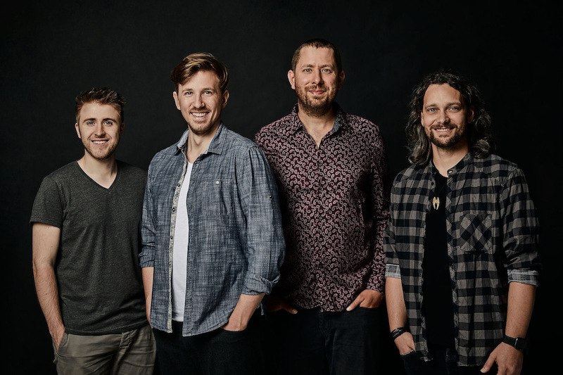 Vier M&auml;nner posieren l&auml;chelnd vor einem dunklen Hintergrund. Sie tragen l&auml;ssige Hemden und T-Shirts., &copy; Interessengemeinschaft Kultur Sindelfingen / B&ouml;blingen e.V.