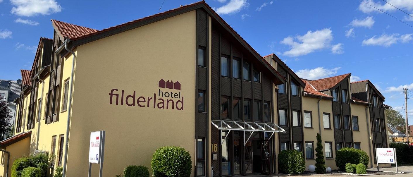 Gelbes Gebäude mit rotem Dach und der Aufschrift 'Hotel Filderland'. Vor dem Gebäude sind Büsche und ein Schild zu sehen., © TOMAS