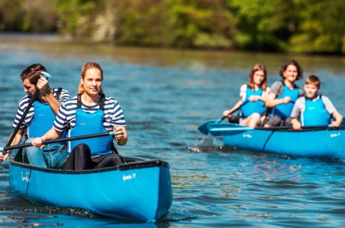Zwei blaue Kanus mit Menschen paddeln auf einem Fluss. Die Personen tragen gestreifte Shirts und blaue Schwimmwesten. Im Hintergrund ist grüne Vegetation., © Cool-Tours StattReisen Zwei blaue Kanus mit Menschen paddeln auf einem Fluss. Die Personen tragen gestreifte Shirts und blaue Schwimmwesten. Im Hintergrund ist grüne Vegetation., © Cool-Tours StattReisen