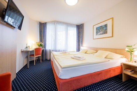 Helles Doppelzimmer mit großem Bett, Schreibtisch, Fernseher an der Wand und Fenster mit Vorhängen. Blumen und Kunstwerk als Dekoration., © Hotel am Schlossberg Herrenberg Helles Doppelzimmer mit großem Bett, Schreibtisch, Fernseher an der Wand und Fenster mit Vorhängen. Blumen und Kunstwerk als Dekoration., © Hotel am Schlossberg Herrenberg