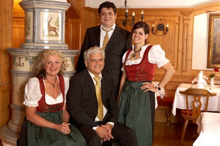 Vier Personen in traditioneller bayerischer Tracht posieren in einem holzgetäfelten Raum mit Kachelofen., © Jeanette Bender Vier Personen in traditioneller bayerischer Tracht posieren in einem holzgetäfelten Raum mit Kachelofen., © Jeanette Bender