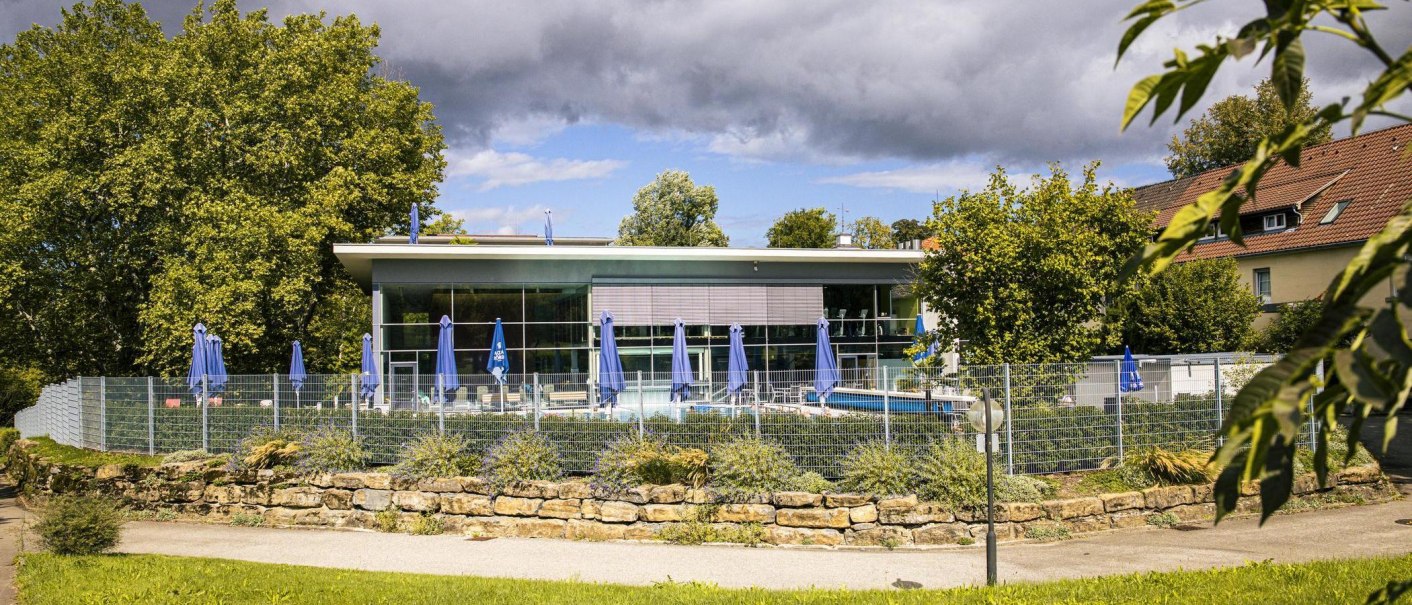 Außenansicht der Mineraltherme Bad Boll, umgeben von Bäumen. Blaue Sonnenschirme stehen auf der Terrasse, ein Zaun umgibt das Gelände., © Stuttgart-Marketing GmbH, Sarah Schmid Außenansicht der Mineraltherme Bad Boll, umgeben von Bäumen. Blaue Sonnenschirme stehen auf der Terrasse, ein Zaun umgibt das Gelände., © Stuttgart-Marketing GmbH, Sarah Schmid
