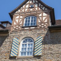 Fachwerkhaus mit blauen Fensterläden, Ziegeldach und grünem Laub im Vordergrund unter blauem Himmel., © Achim Mende