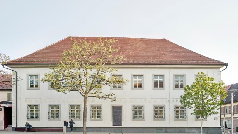 Ein zweist&ouml;ckiges Geb&auml;ude mit wei&szlig;er Fassade und rotem Dach, flankiert von zwei B&auml;umen, steht an einer Stra&szlig;e. Zwei Personen sind vor dem Geb&auml;ude zu sehen., &copy; Ludwigsburg Museum