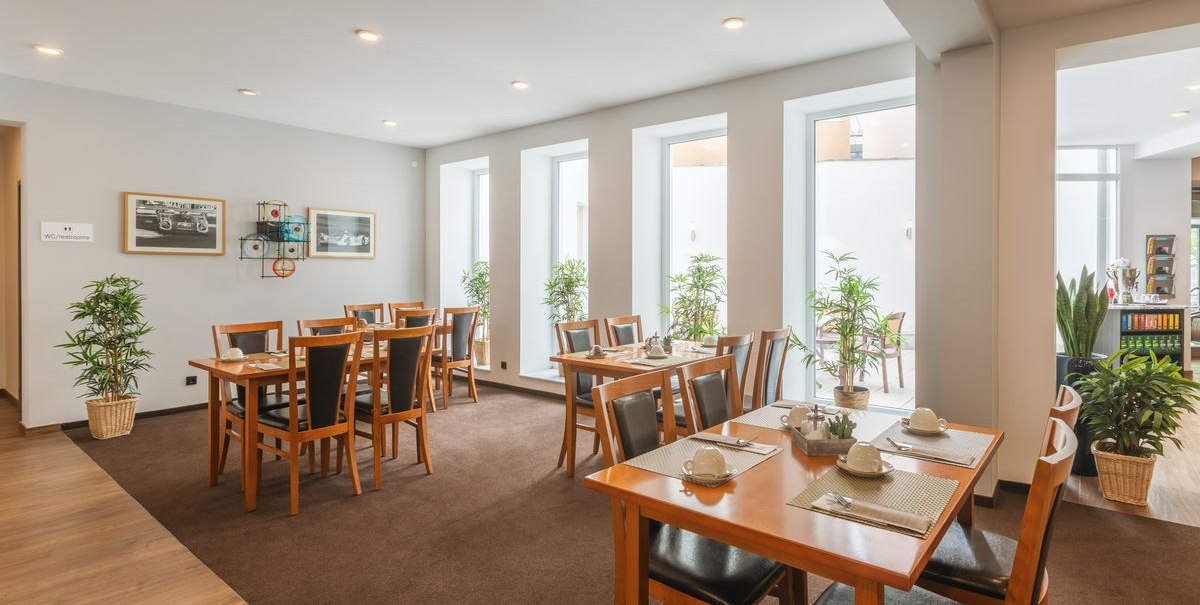 Ein heller Speiseraum mit Holztischen und Stühlen, Pflanzen und Bildern an der Wand. Große Fenster lassen viel Licht herein., © Novum Hospitality