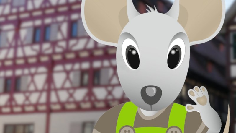 Eine animierte Maus namens Herri in gr&uuml;ner Latzhose steht vor einem Fachwerkgeb&auml;ude. Die Maus winkt freundlich., &copy; Stadt Herrenberg