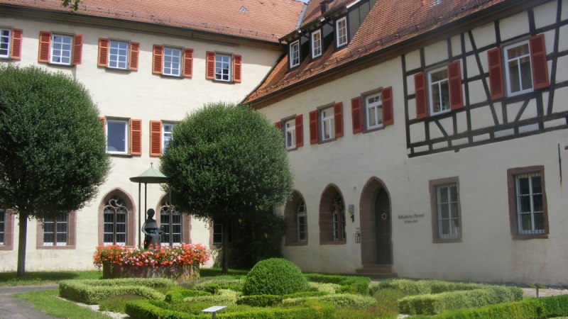 Historisches Gebäude mit Fachwerk und rotem Dach in Bad Mergentheim. Gepflegter Garten mit Brunnen und Blumen im Vordergrund., © Natur.Nah. Schönbuch & Heckengäu Historisches Gebäude mit Fachwerk und rotem Dach in Bad Mergentheim. Gepflegter Garten mit Brunnen und Blumen im Vordergrund., © Natur.Nah. Schönbuch & Heckengäu