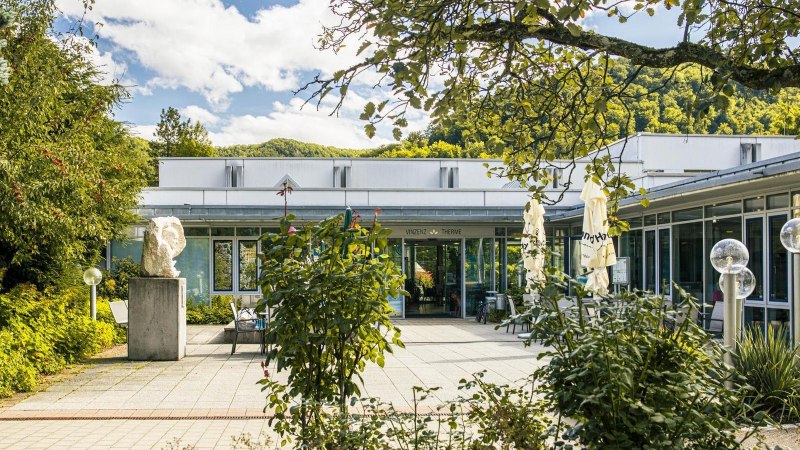 Eingang der Vinzenz Therme in Bad Ditzenbach, umgeben von üppigem Grün und einem sonnigen Himmel., © SMG, Sarah Schmid Eingang der Vinzenz Therme in Bad Ditzenbach, umgeben von üppigem Grün und einem sonnigen Himmel., © SMG, Sarah Schmid