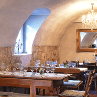 Gemütlicher Gastraum mit gedeckten Holztischen, Kronleuchter, Spiegel und rustikalen Steinwänden. Elegante Atmosphäre mit Kerzen und Blumen., © FreCla Gastronomiebetriebe GmbH