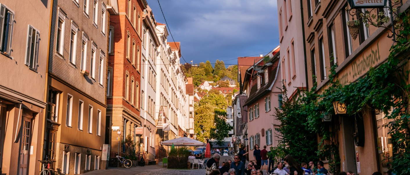 Straßenszene im Bohnenviertel mit historischen Gebäuden, Menschen in Straßencafés und grünem Laub. Die Abendsonne beleuchtet die Fassaden., © SMG Thomas Niedermüller