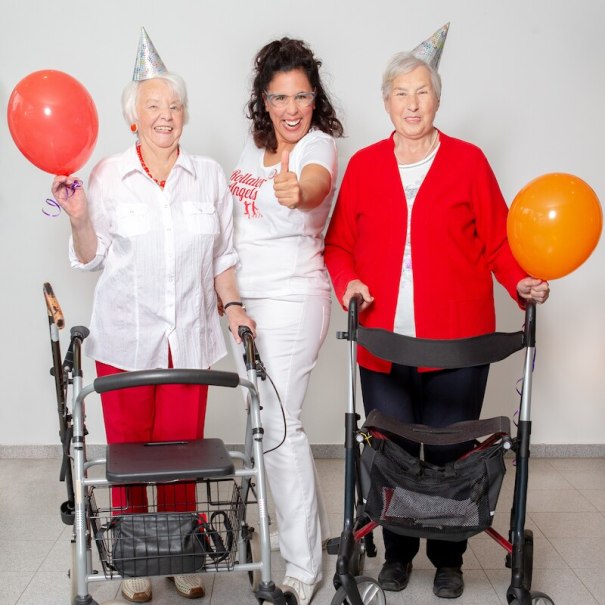 Drei Frauen feiern mit Luftballons und Partyh&uuml;ten. Zwei &auml;ltere Damen mit Rollatoren, die mittlere Frau zeigt Daumen hoch. Fr&ouml;hliche Stimmung., &copy; Mauerwerk GmbH
