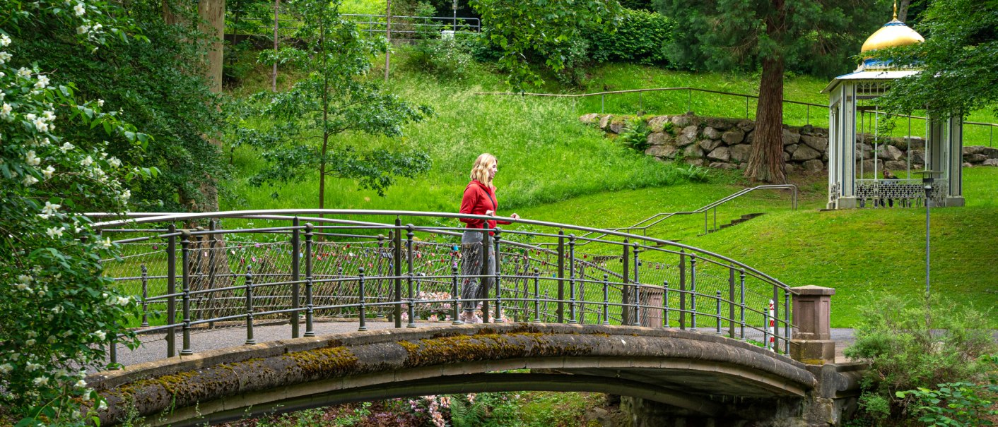 Frau auf einer Brücke im grünen Park neben einem Pavillon mit goldener Kuppel., © Lightworkart, Touristik Bad Wildbad GmbH Frau auf einer Brücke im grünen Park neben einem Pavillon mit goldener Kuppel., © Lightworkart, Touristik Bad Wildbad GmbH