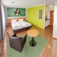Modernes Superior Doppelzimmer mit zwei Betten, grünem Wandbild, Tisch, Stuhl und kleiner Küchenzeile auf Holzboden., © attimo Hotel Stuttgart Modernes Superior Doppelzimmer mit zwei Betten, grünem Wandbild, Tisch, Stuhl und kleiner Küchenzeile auf Holzboden., © attimo Hotel Stuttgart