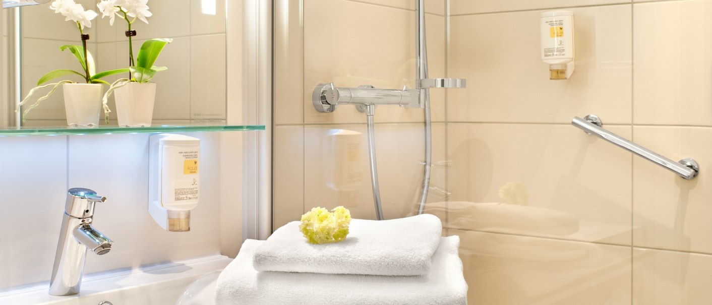 Modernes Badezimmer mit Dusche, Waschbecken, weißen Handtüchern und Orchideen auf einem Regal., © TOMAS