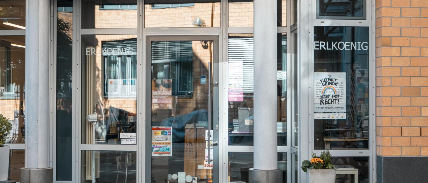 Eingang eines Gebäudes mit Glastüren, auf denen 'ERLKOENIG' steht. Poster und Pflanzen sind sichtbar. Moderne Architektur mit Backsteinfassade., © SMG, Sarah Schmid Eingang eines Gebäudes mit Glastüren, auf denen 'ERLKOENIG' steht. Poster und Pflanzen sind sichtbar. Moderne Architektur mit Backsteinfassade., © SMG, Sarah Schmid