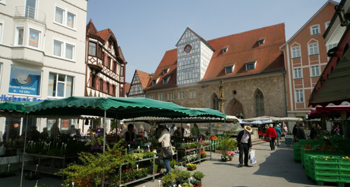 Wochenmarkt in Reutlingen mit Verkaufsständen und Besuchern. Im Hintergrund sind historische Gebäude und der Spitalhof zu sehen., © Sphäre Verlag Wochenmarkt in Reutlingen mit Verkaufsständen und Besuchern. Im Hintergrund sind historische Gebäude und der Spitalhof zu sehen., © Sphäre Verlag