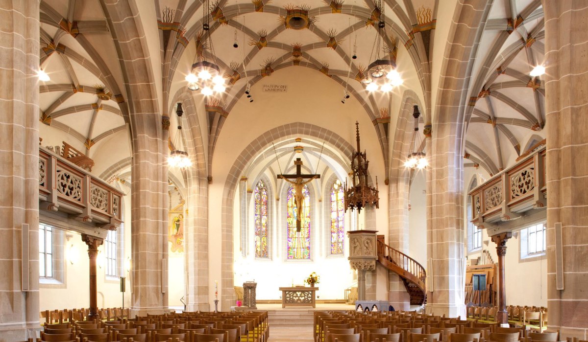 Innenansicht der Michaelskirche mit gotischen Bögen, Buntglasfenstern und Holzbänken. Der Altarbereich ist zentral im Bild., © Remstal Tourismus e.V.