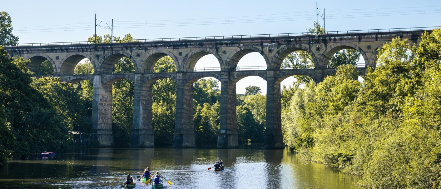 Viadukt in Bietigheim-Bissingen über einem Fluss. Mehrere Kanufahrer paddeln unter der Brücke. Umgeben von grünen Bäumen und klarem Himmel., © Stuttgart Marketing GmbH, Sarah Schmid