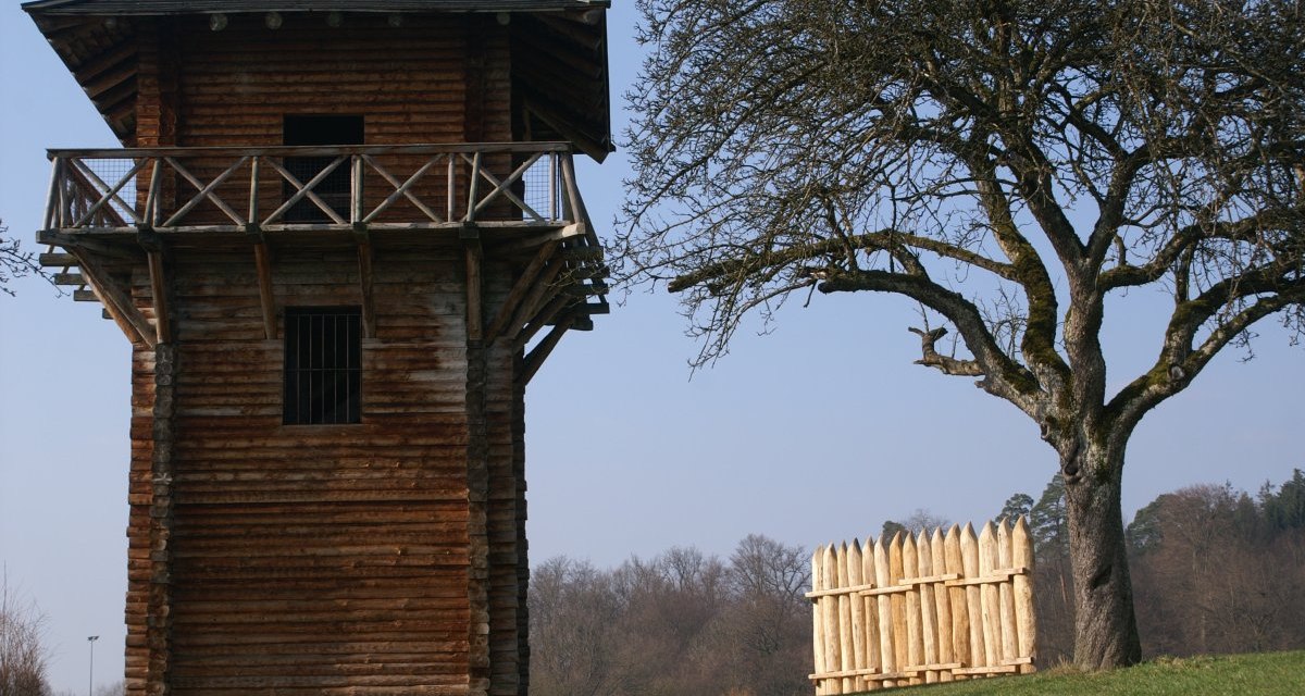 Ein hölzerner römischer Wachturm steht neben einem kahlen Baum und einem kleinen Holzzaun auf einer grünen Wiese., © Remstal Tourismus e.V. Ein hölzerner römischer Wachturm steht neben einem kahlen Baum und einem kleinen Holzzaun auf einer grünen Wiese., © Remstal Tourismus e.V.