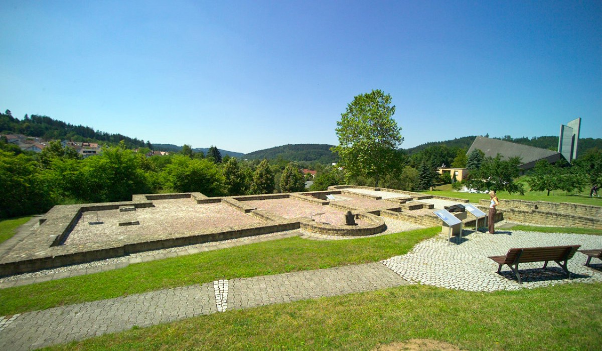 Ruinen des Kastellbads Schirenhof mit Informationstafeln, einer Person und einer modernen Kirche im Hintergrund. Grüne Landschaft und blauer Himmel., © Stadtverwaltung Schwäbisch Gmünd Ruinen des Kastellbads Schirenhof mit Informationstafeln, einer Person und einer modernen Kirche im Hintergrund. Grüne Landschaft und blauer Himmel., © Stadtverwaltung Schwäbisch Gmünd