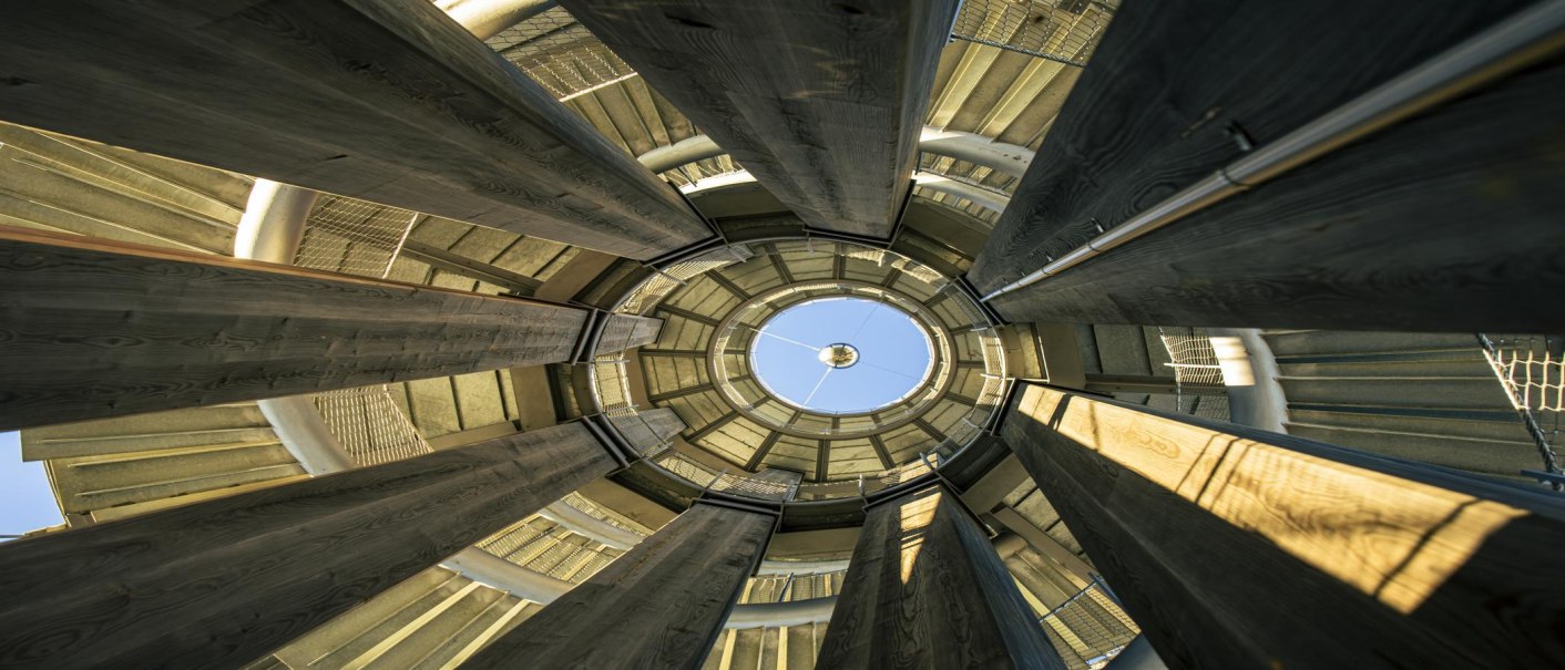 Blick nach oben im Schönbuchturm, zeigt kreisförmige Holz- und Metallstrukturen, die sich zur blauen Himmelöffnung hin verjüngen., © SMG, Sarah Schmid