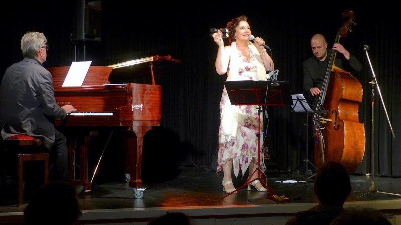 Eine Sängerin performt auf einer Bühne, begleitet von einem Pianisten am Flügel und einem Kontrabassisten. Die Atmosphäre ist intim und musikalisch., © Foto Jazzclub Ludwigsburg Eine Sängerin performt auf einer Bühne, begleitet von einem Pianisten am Flügel und einem Kontrabassisten. Die Atmosphäre ist intim und musikalisch., © Foto Jazzclub Ludwigsburg