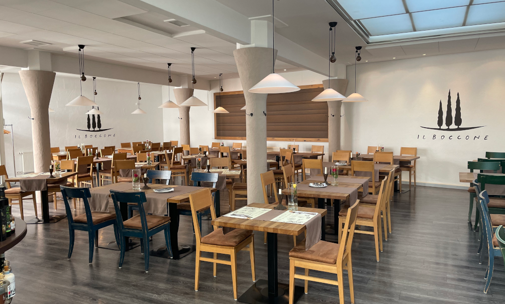 Leeres Restaurant 'Il Boccone' mit Holztischen und St&uuml;hlen, stilvollen Lampen und einem Logo an der Wand. Modernes, einladendes Ambiente., &copy; Restaurant Il Boccone