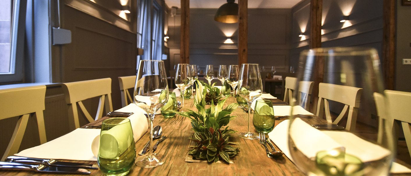 Ein stilvoll gedeckter Esstisch mit Weingläsern, grünen Gläsern und Pflanzen als Dekoration in einem eleganten Raum., © Classic Rock Café Gastronomie- Betriebs GmbH