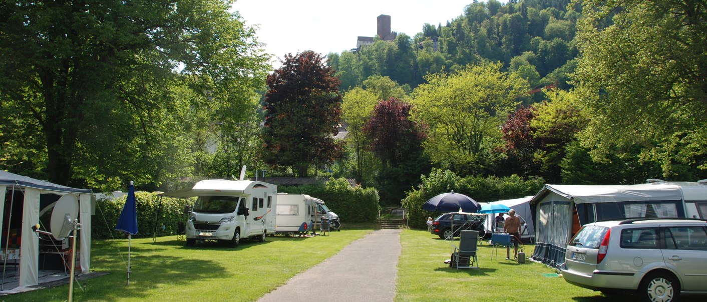 Campingplatz mit Wohnmobilen und Zelten, umgeben von grünen Bäumen und Hügeln. Im Hintergrund ist eine Burg auf einem Hügel zu sehen., © Campingpark Bad Liebenzell, Andreas Harter