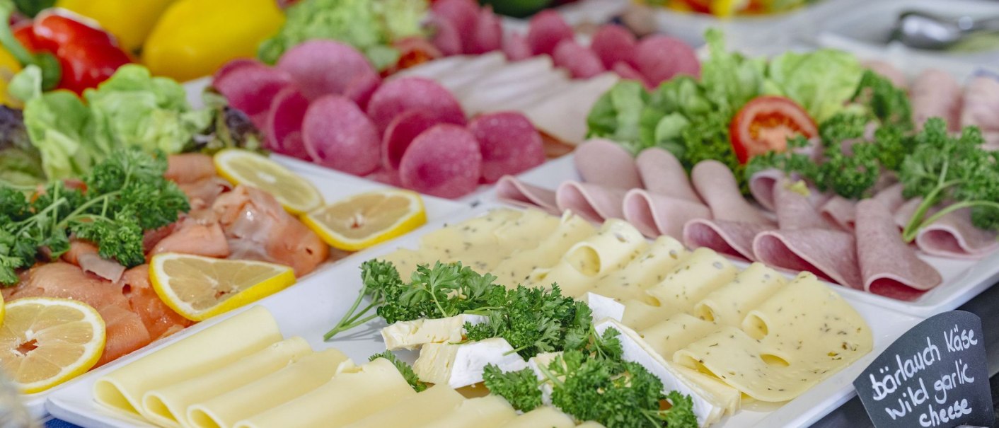 Ein Frühstücksbuffet mit verschiedenen Käsesorten, Wurst, Lachs, Zitronenscheiben und frischem Gemüse auf einem Tisch arrangiert., © Plaza INN Stuttgart-Filderstadt Ein Frühstücksbuffet mit verschiedenen Käsesorten, Wurst, Lachs, Zitronenscheiben und frischem Gemüse auf einem Tisch arrangiert., © Plaza INN Stuttgart-Filderstadt