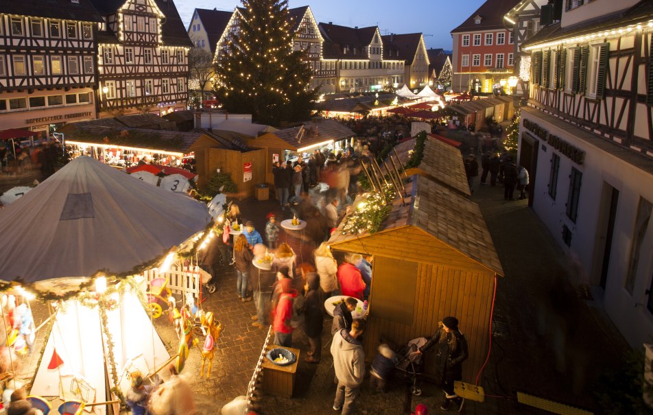 Ein festlich beleuchteter Weihnachtsmarkt mit Fachwerkhäusern, Ständen und einem großen Weihnachtsbaum. Menschen schlendern und genießen die Atmosphäre., © Stadt Schorndorf Ein festlich beleuchteter Weihnachtsmarkt mit Fachwerkhäusern, Ständen und einem großen Weihnachtsbaum. Menschen schlendern und genießen die Atmosphäre., © Stadt Schorndorf