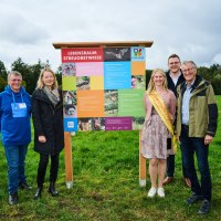 F&uuml;nf Personen posieren vor einem bunten Informationsschild mit der Aufschrift 'Lebensraum Streuobstwiese' auf einer gr&uuml;nen Wiese., &copy; Natur.Nah. Sch&ouml;nbuch & Heckeng&auml;u