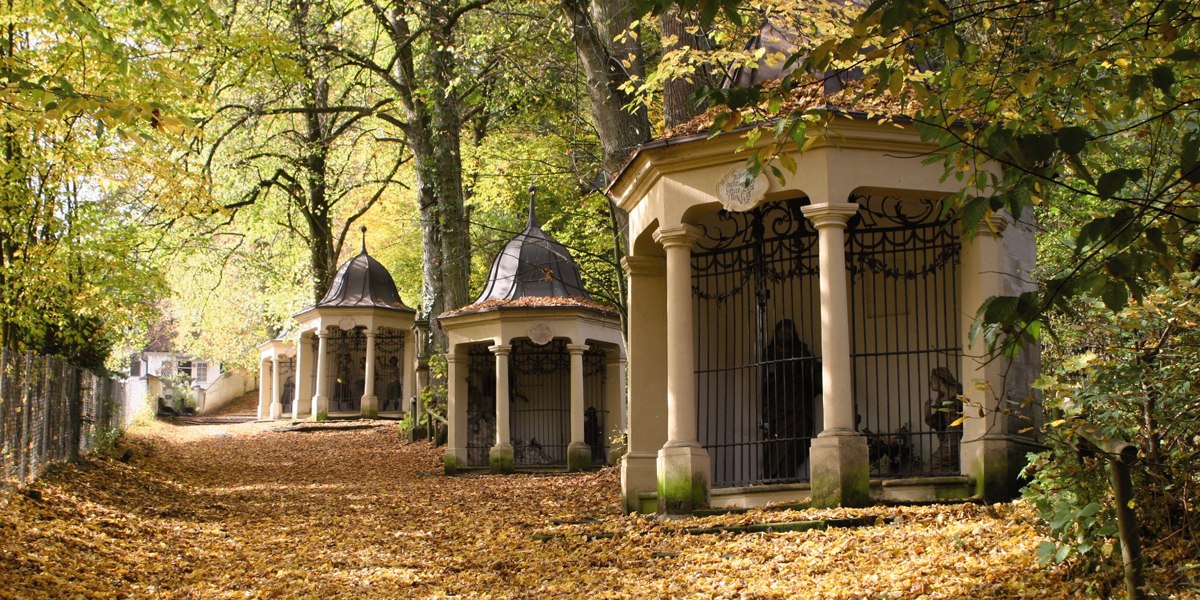 Ein herbstlicher Weg, bedeckt mit Laub, führt an kleinen Kapellen vorbei, umgeben von Bäumen., © Touristik und Marketing GmbH Schwäbisch Gmünd