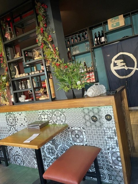 Stilvolle Bar mit gemusterten Fliesen, Pflanzen und Regalen mit Flaschen. Ein Tisch mit Hocker steht im Vordergrund., © cAvada Stilvolle Bar mit gemusterten Fliesen, Pflanzen und Regalen mit Flaschen. Ein Tisch mit Hocker steht im Vordergrund., © cAvada