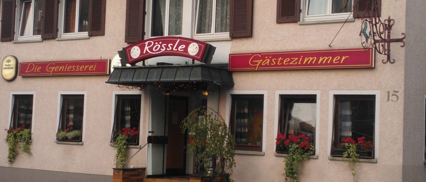 Gasthaus Rössle in Urbach mit Schildern 'Die Geniesserei' und 'Gästezimmer', Blumenkästen an den Fenstern und einer Eingangstreppe., © Gasthaus Rössle