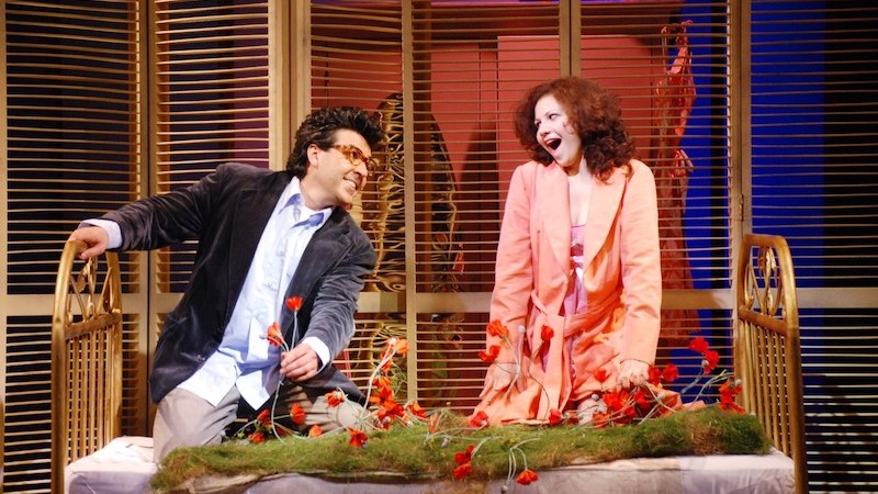 Zwei Operns&auml;nger auf einer B&uuml;hne in einer lebhaften Szene aus Rossinis "La Scala di seta". Sie sitzen auf einem Bettgestell, umgeben von Blumen., &copy; Touristik Bad Wildbad GmbH