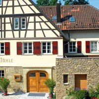 Fachwerkhaus mit rotem Dach und Fensterläden, beschriftet mit 'Jagstmühle'. Vor dem Haus stehen Pflanzen in Töpfen., © Landgasthof + Hotel Jagstmühle Fachwerkhaus mit rotem Dach und Fensterläden, beschriftet mit 'Jagstmühle'. Vor dem Haus stehen Pflanzen in Töpfen., © Landgasthof + Hotel Jagstmühle