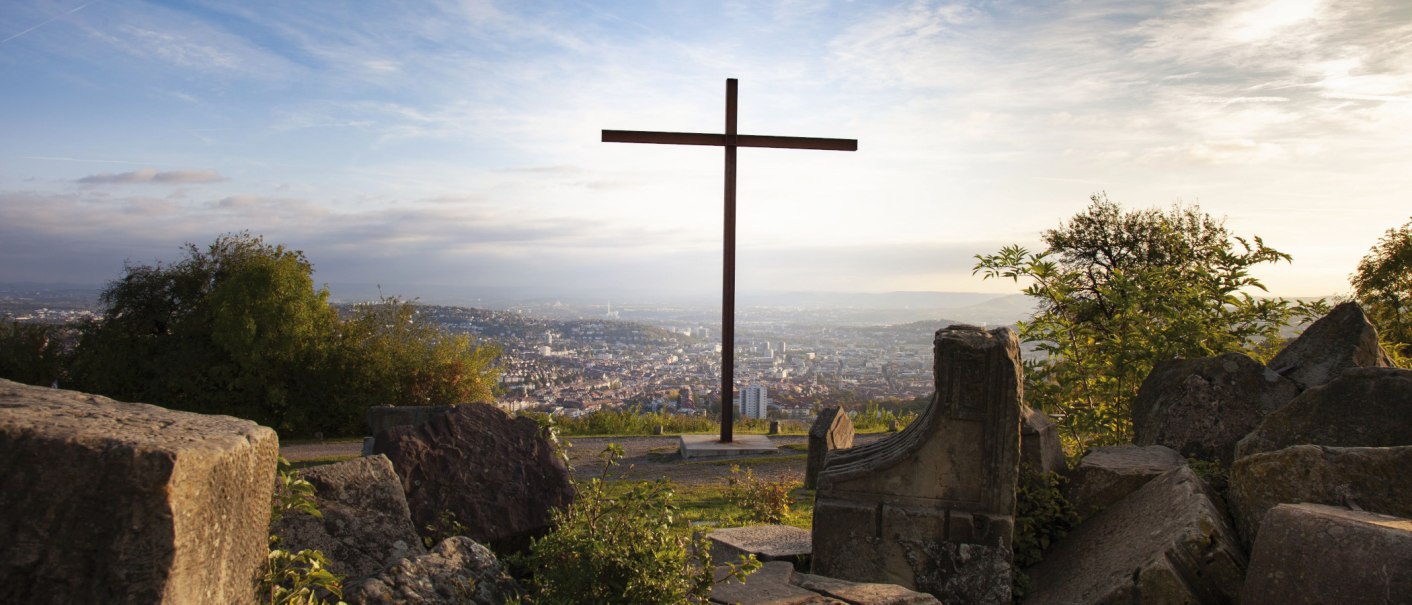 Ein Kreuz auf dem Birkenkopf in Stuttgart, umgeben von Trümmern, mit Blick auf die Stadt im Hintergrund bei Sonnenuntergang., © Stuttgart-Marketing GmbH, Jean-Claude Winkler Ein Kreuz auf dem Birkenkopf in Stuttgart, umgeben von Trümmern, mit Blick auf die Stadt im Hintergrund bei Sonnenuntergang., © Stuttgart-Marketing GmbH, Jean-Claude Winkler