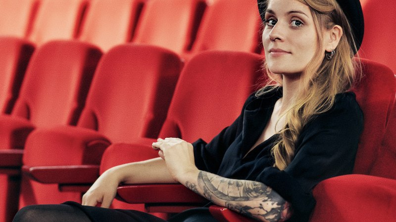 Eine Person mit Hut und t&auml;towiertem Arm sitzt entspannt in einem leeren Kinosaal auf einem roten Sitz., &copy; Mauerwerk GmbH