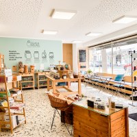 Ein heller Unverpackt-Laden mit Regalen voller Produkte, Tischen und einer gro&szlig;en Fensterfront. An der Wand steht "Glas & Beutel"., &copy; cGlasundBeutel