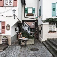 Schmale Gasse in einer Altstadt mit Fachwerkhäusern, Pflanzen in Töpfen und dekorativen Schildern. Kopfsteinpflaster und Treppenstufen., © Martina Naumov