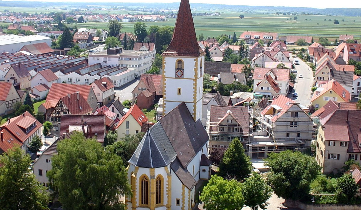Luftaufnahme von Holzgerlingen mit einer Kirche im Vordergrund, umgeben von Häusern und grüner Landschaft im Hintergrund., © Natur.Nah. Schönbuch & Heckengäu Luftaufnahme von Holzgerlingen mit einer Kirche im Vordergrund, umgeben von Häusern und grüner Landschaft im Hintergrund., © Natur.Nah. Schönbuch & Heckengäu