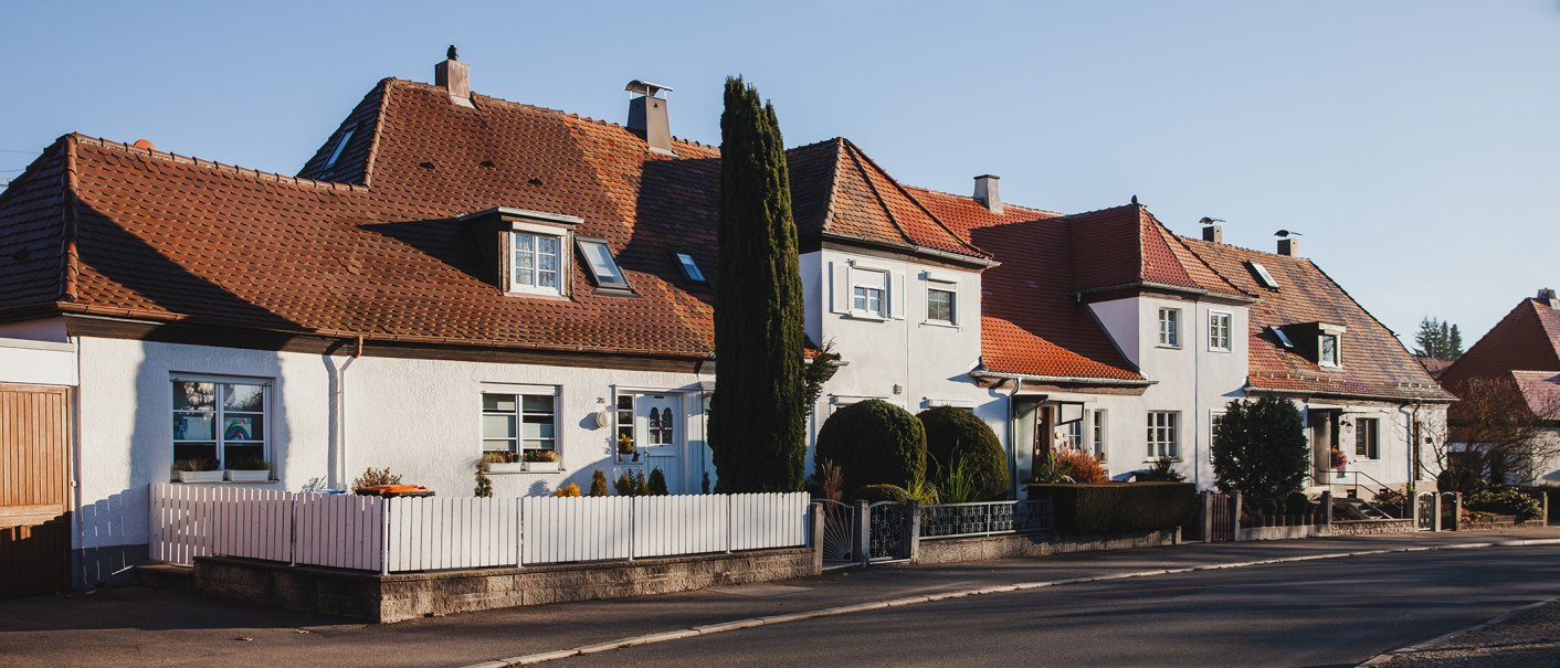 Reihenhäuser mit roten Ziegeldächern und weißen Fassaden in einer ruhigen Wohnsiedlung bei Sonnenschein., © benjaminknoblauch.de